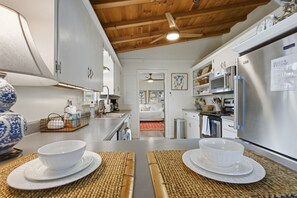 A modern kitchen with white cabinets, stainless steel appliances, and a wooden ceiling.
