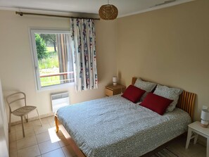 A bedroom with a bed, a chair, a bedside table, a lamp, and a window with curtains. - Spacious apartment with pool (Saint-Raphaël)
