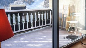 A balcony with a view of snow-covered mountains, a red chair, and a glass door leading to a room with a white chair and a small table. - Lovely T3 with loggias close to the slopes (Saint-Chaffrey)