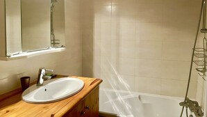 A bathroom with a wooden vanity, a white sink, a mirror, and a shower area.