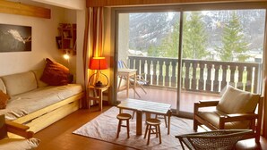 A cozy living room with a sofa, a table with two stools, a lamp, and a view of a balcony with a railing. - Lovely T3 with loggias close to the slopes (Saint-Chaffrey)