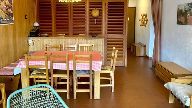 A cozy room with a wooden dining table set for four, a wicker chair, a bench, and a hanging light fixture. - Lovely T3 with loggias close to the slopes (Saint-Chaffrey)