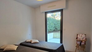 Habitación con dos camas, una pequeña silla de madera y un ventanal corredero que da a un espacio exterior.