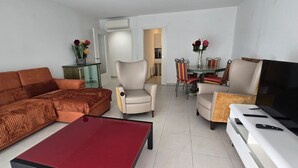 Una sala de estar con sofá, sillones, una mesa de centro, televisor y una mesa de comedor con sillas.