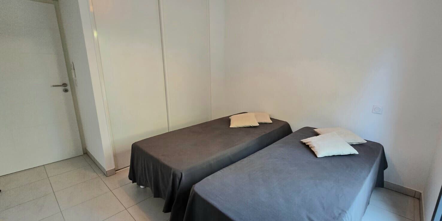 A small, clean room with two single beds, a door, and a tiled floor.
