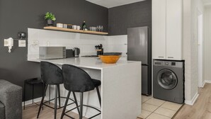 A modern kitchen with a central island, black bar stools, a washing machine, and a small plant on the wall. - Stylish De Waterkant Escape Pool andPrime Location (Cape Town)
