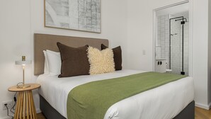 A neatly made bed with a green throw, a bedside lamp, and a framed abstract painting on the wall. - Ratanga Park Escape | Century City (Cape Town)