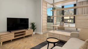 A modern living room with a flat-screen TV, wooden furniture, a large window, and a view of the city. - Modern Foreshore Apartment | Mountain Views (Cape Town)