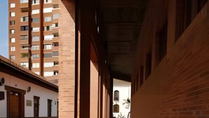 A corridor with brick walls and a tiled floor, leading to a building with a white facade and a wooden door. - Willis (Cali)