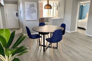 Ein Essbereich mit einem runden Tisch, blauen Stühlen, einer hängenden Pendelleuchte und einer großen Pflanze.