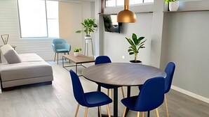 A modern living room with a round dining table, blue chairs, a sofa, and potted plants. - Willis (Cali)