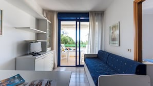 A room with a bed, a desk with a computer, a chair, a sofa, a window with curtains, and a balcony with outdoor furniture. - Great Apartment With Stunning Terrace in Bibione (San Michele al Tagliamento)