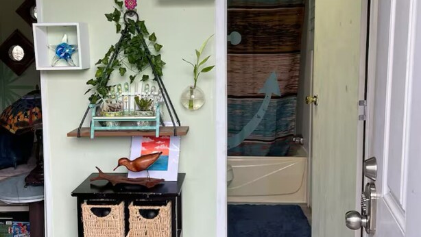 Un pasillo con una puerta que da a un baño, un pequeño estante con objetos decorativos y una exhibición de cestas tejidas.