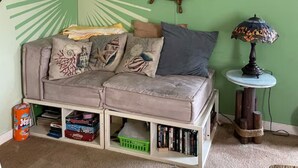 Una habitación acogedora con pared verde, una rueda de barco de madera, una mesita con lámpara y un sofá con cojines decorativos.