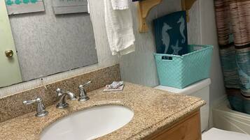 A bathroom with a granite countertop sink, wooden cabinets, a towel rack, and a toilet.