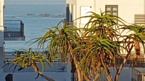 A coastal building with a curved roof, a balcony with a railing, and a view of the sea. - Two Bedroom Beachfront Penthouse with Parking (Cape Town)