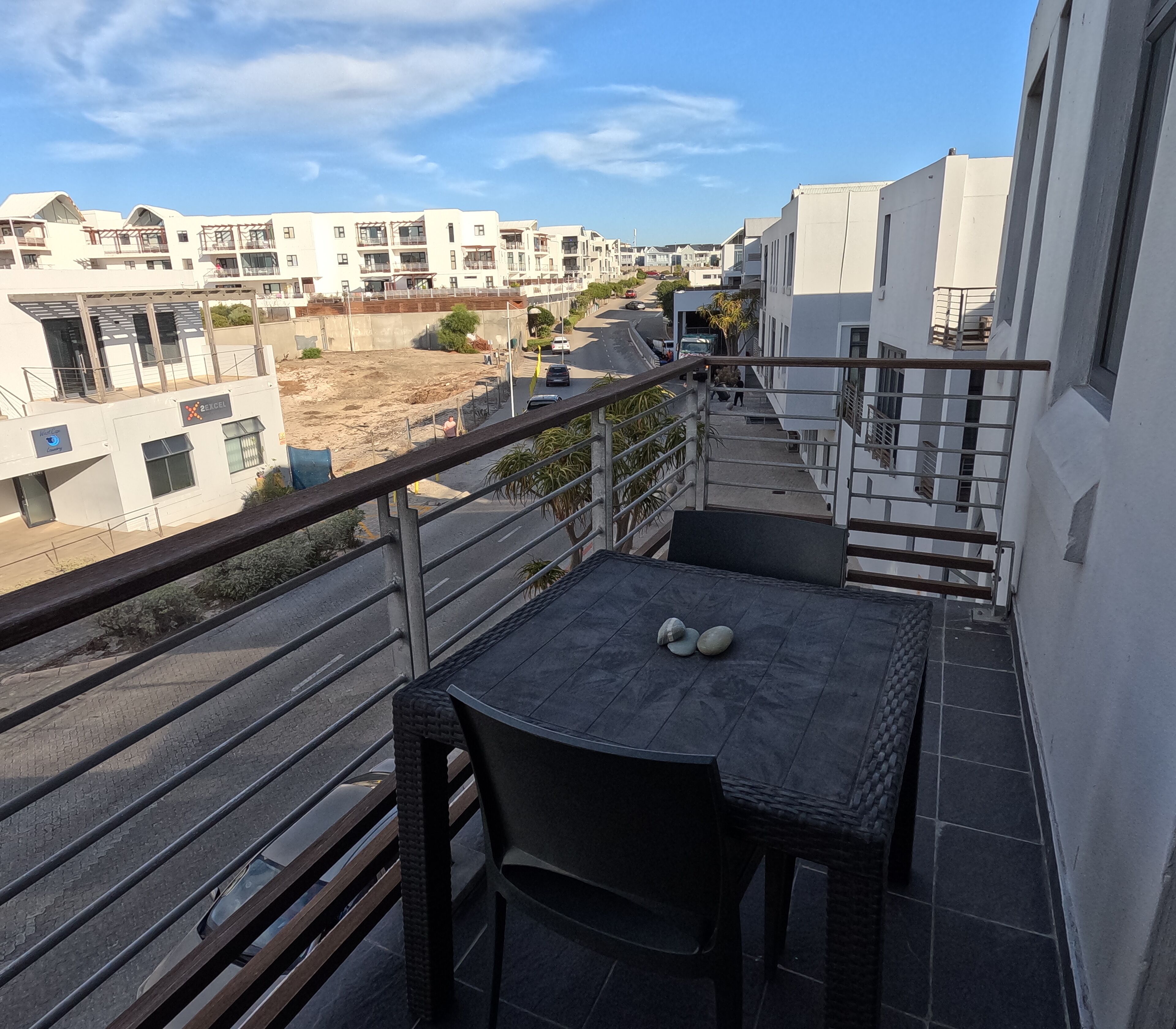 Un balcon avec une table et des chaises, donnant sur un quartier résidentiel avec des immeubles modernes.