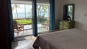 A bedroom with a bed, a dresser, a chair, and a view of the ocean.