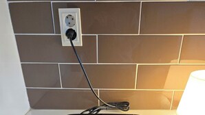 A black electronic device, possibly a thermostat, mounted on a wall with a power outlet above it.