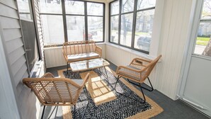 A sunlit room with a glass table and wicker chairs, large windows, and a patterned rug. - Two Bedroom Home close to Downtown and Hospitals (Sioux Falls)