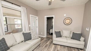 A living room with two beige sofas, patterned cushions, a wooden floor, a ceiling fan, and a wall clock. - Two Bedroom Home close to Downtown and Hospitals (Sioux Falls)