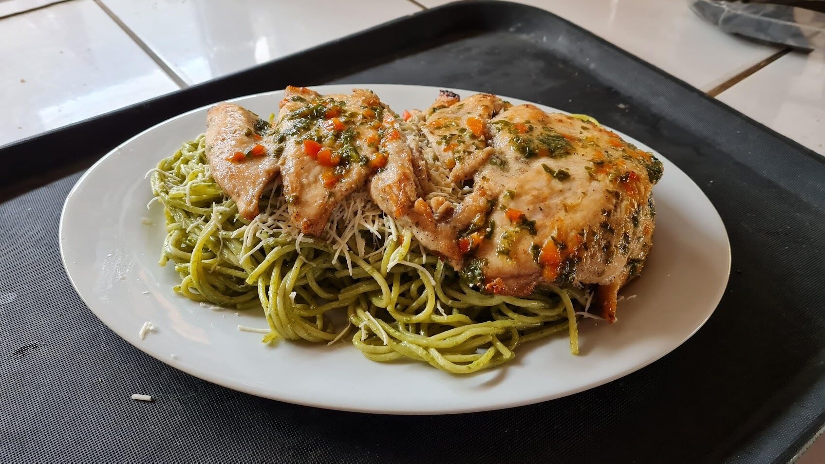 Un plato de espagueti con pollo sobre una bandeja negra.