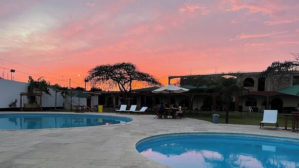 A swimming pool area with lounge chairs and a sunset sky. - HOSPEDAJE EL CASCABEL (Sunampe)