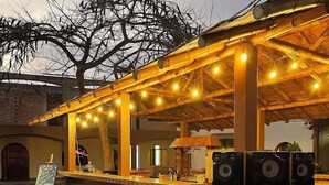 An outdoor bar with a brick counter, wooden chairs, and string lights. - HOSPEDAJE EL CASCABEL (Sunampe)