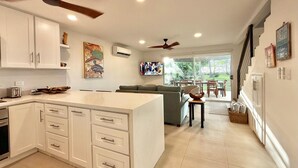A modern kitchen with white cabinets, a central island, and a dining area with a green sofa and a TV. - 37 steps to Playa Potrero from the back door. Pool, Sleeps 6! Sunsets galore! (Guanacaste Province)