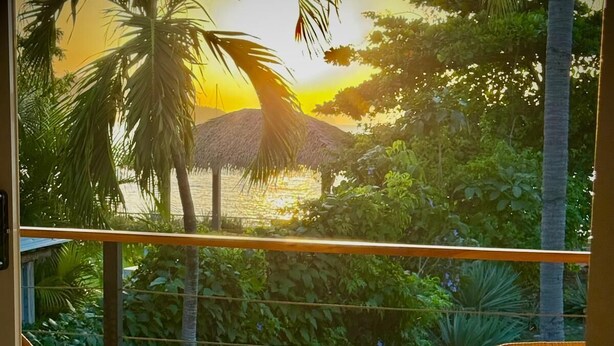 A balcony with wicker chairs and a table, two glasses of beer, and a tropical view. - 37 steps to Playa Potrero from the back door. Pool, Sleeps 6! Sunsets galore! (Guanacaste Province)