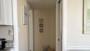 A hallway with a kitchen area on the left, a wicker chair with a cushion, and a gray sofa on the right. - Lovers’ Key Beach Club by Check In Vacation Rental - 1 Bedroom Apartment #1005 (Bonita Springs)