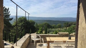 An outdoor terrace with a stone wall, a wooden table, and white chairs.