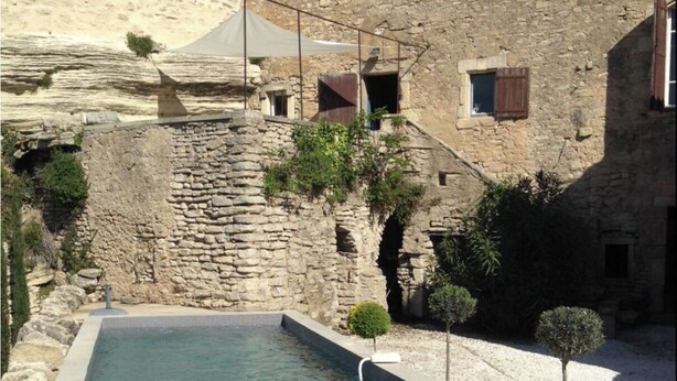 A stone building with a swimming pool, a small garden, and a stone wall.