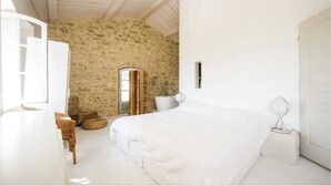 A bedroom with a stone wall, a white bed, a white sink, and a white door.