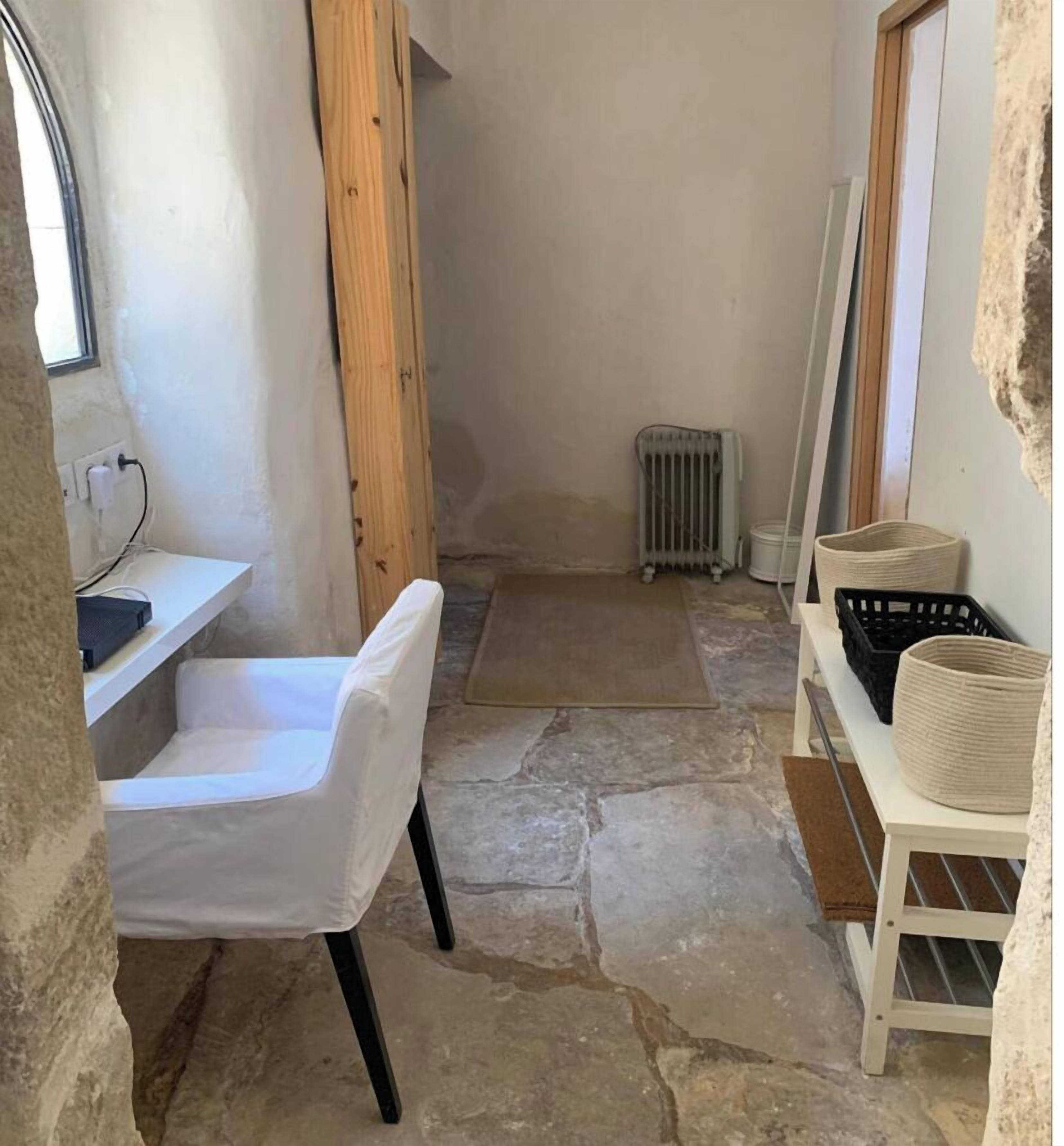 A narrow stone-floored room with a white chair, a radiator, and storage baskets on shelves.
