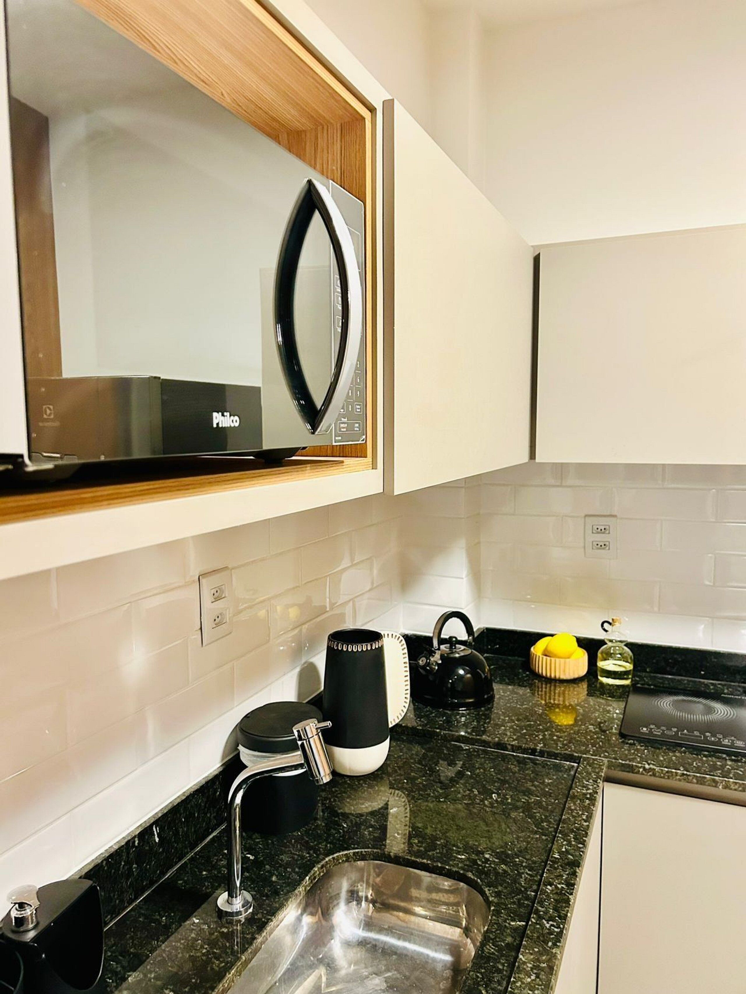A kitchen with a microwave, kettle, and coffee maker on the counter, a sink, and a cabinet above the counter.