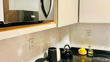 Una cocina con microondas, hervidor y cafetera sobre la encimera, un fregadero y un armario encima.