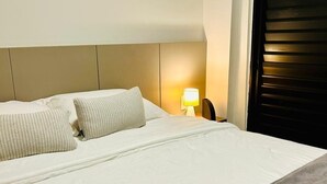 Une chambre d’hôtel avec un lit, des oreillers, une table de chevet avec une lampe et une porte de couleur sombre.