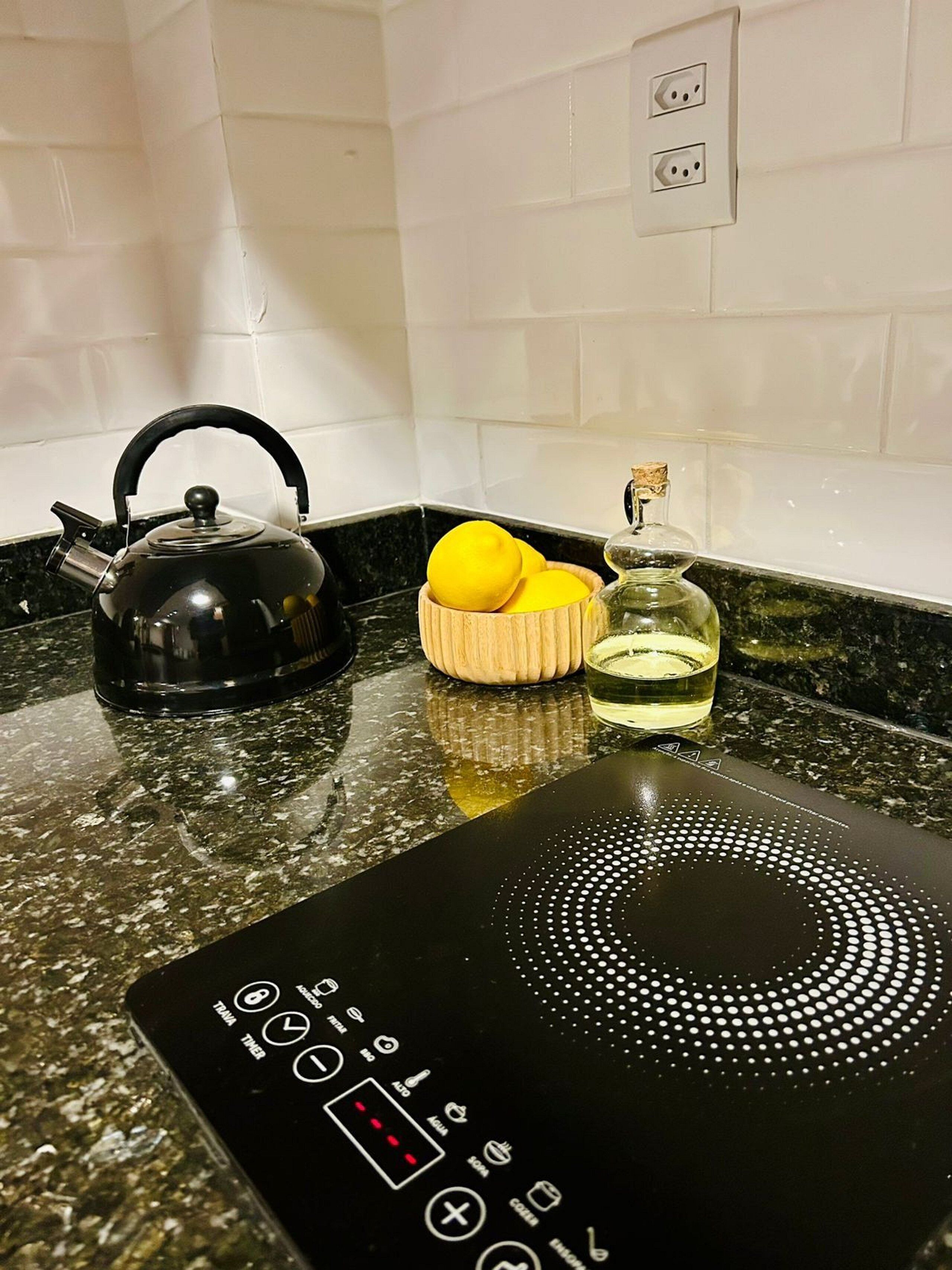 A kitchen with a black induction cooktop, a kettle, lemons, and a glass jar.