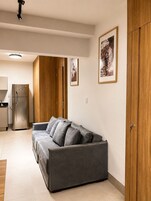 Un espacio moderno para vivir con un sofá gris, un armario de madera y una zona de cocina con refrigerador.