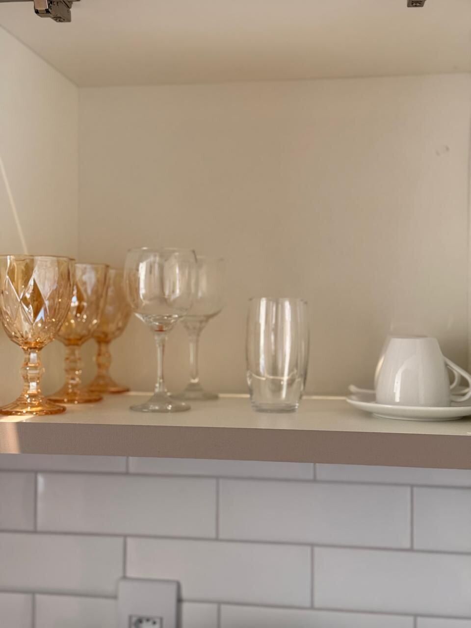 Una encimera de cocina con diferentes vasos y una taza blanca sobre un salpicadero de azulejos blancos.