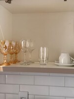 Una encimera de cocina con diferentes vasos y una taza blanca sobre un salpicadero de azulejos blancos.