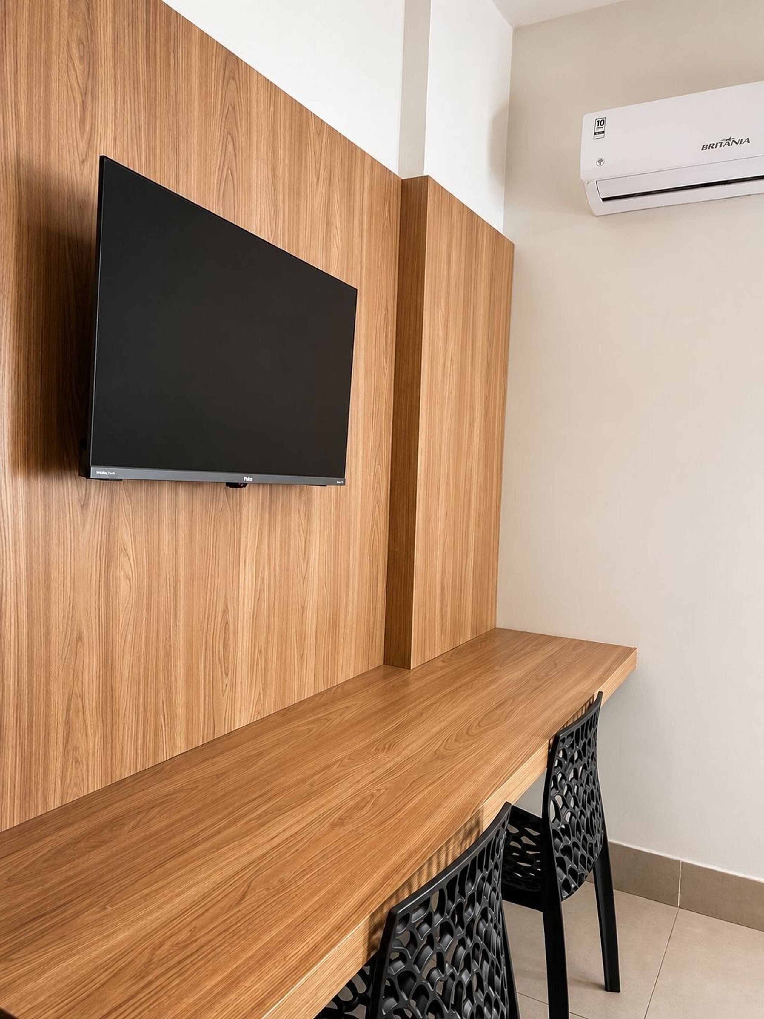 A modern room with a wooden wall panel, a mounted flat-screen TV, a wooden table, and a black chair.