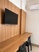 Habitación moderna con paneles de madera, televisor de pantalla plana montado, una mesa de madera y una silla negra.