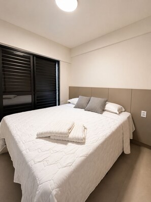 Un dormitorio con una cama grande, cabecera, ventana con persianas y una lámpara en el techo.