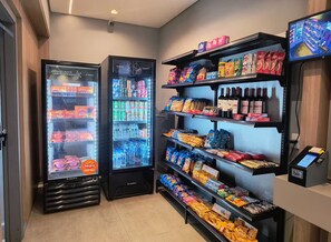 Eine Selbstbedienungs-Getränkestation mit gekühlten und ungekühlten Optionen, Regale voller Snacks und einem Bezahlsystem.