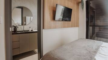 A modern bedroom with a bed, a TV mounted on a wooden panel, a bathroom with a marble wall, and a large window.