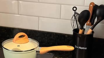 Una cocina con una olla de vidrio sobre una cocina de inducción, una cuchara de mango de madera y un portalapices con utensilios negros y de madera.