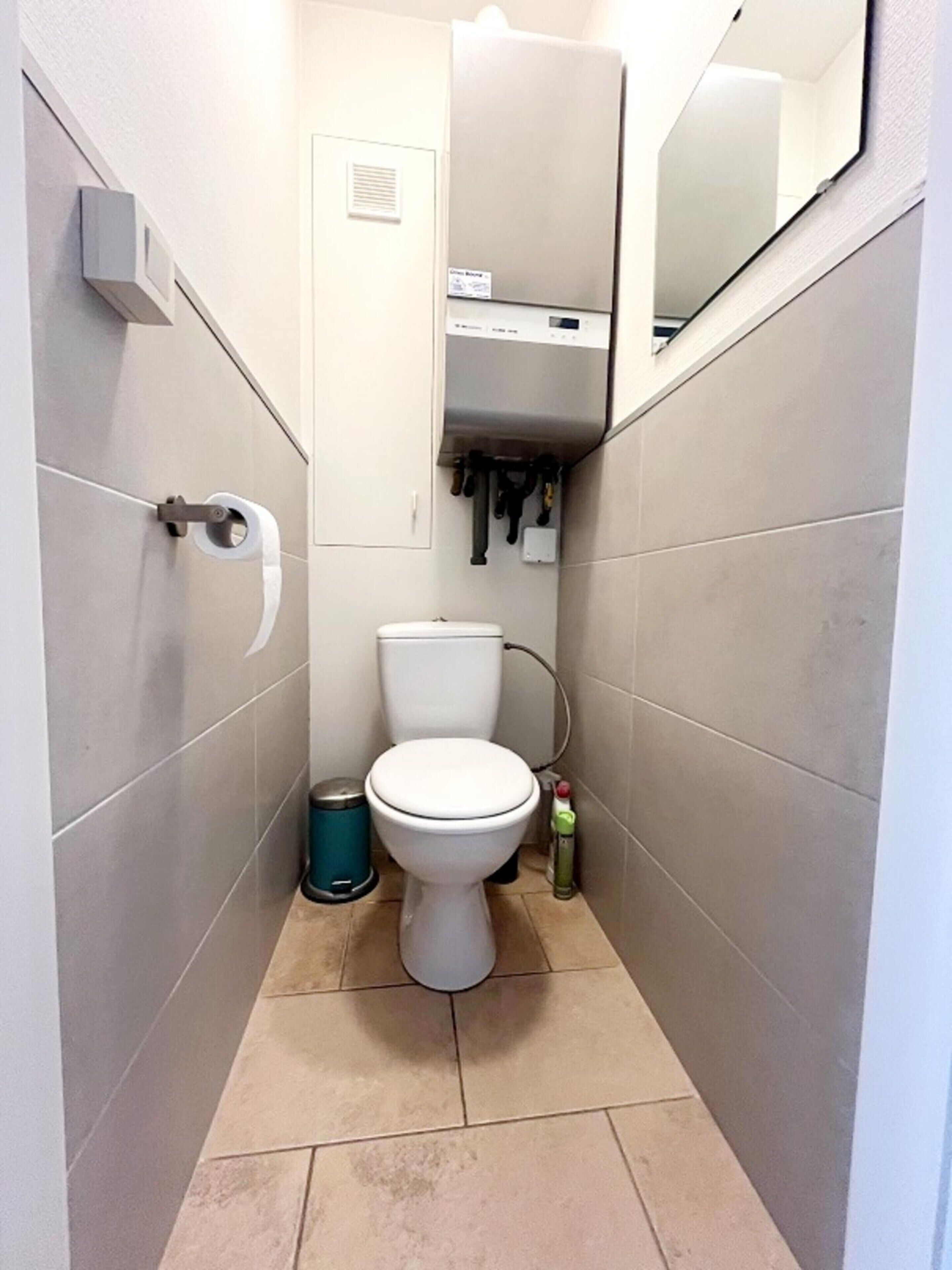 A small, narrow bathroom with a toilet, a trash bin, and a hand dryer.