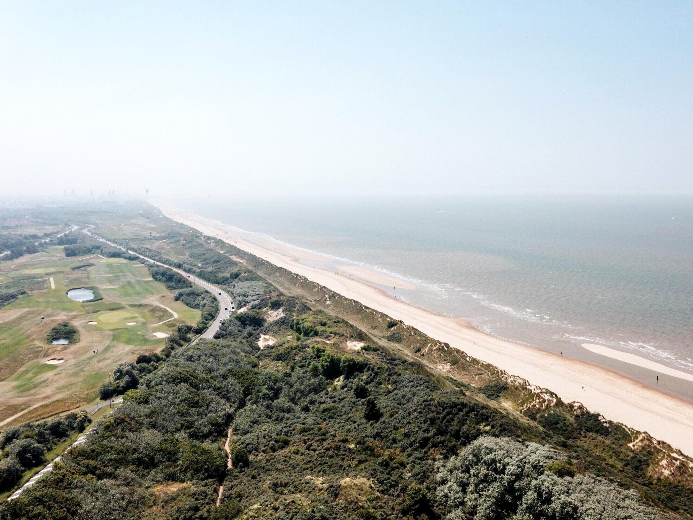 A coastal landscape with a beach, a golf course, and a road.
